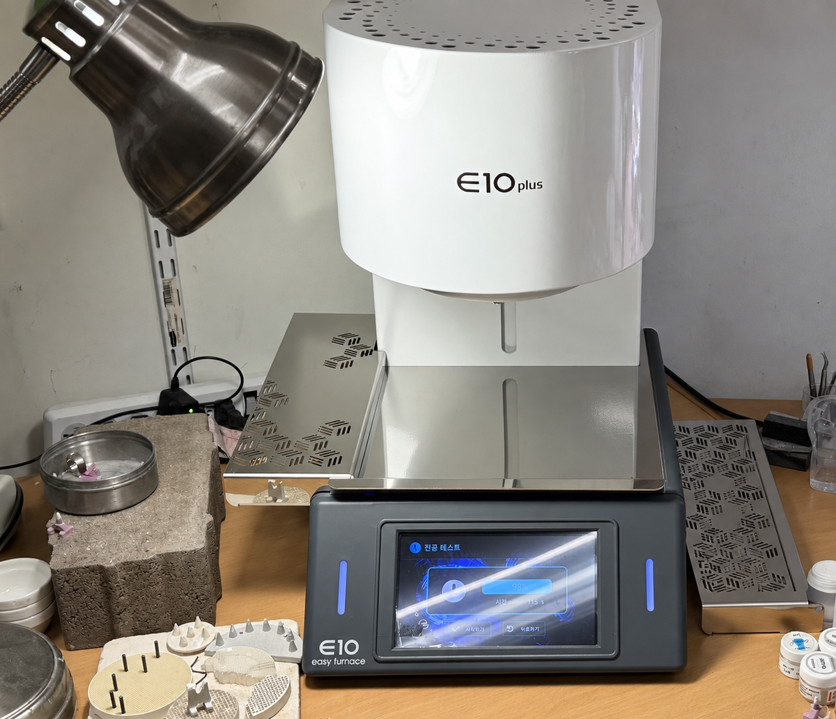 E10 Plus dental porcelain furnace installed in a lab workspace, with vacuum test displayed on the touchscreen